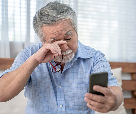 Man using smartphone and rubbing his eye